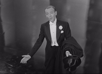 Movie still from “Swing Time” (1936), directed by George Stevens – A black and white photo of a man in a tuxedo holding a suit case; Medium shot, High angle