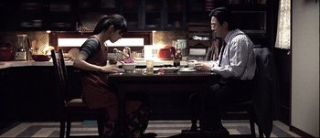 Movie still from “Sympathy for Lady Vengeance” (2005) – A man and a woman sitting at a dinner table; Wide shot, High angle