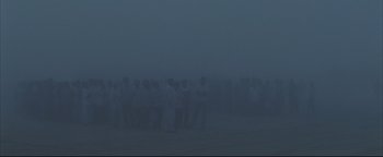 Movie still from “Syriana” (2005), directed by Stephen Gaghan – A large group of people standing in the middle of a foggy field; Extreme Wide shot, High angle