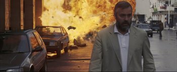 Movie still from “Syriana” (2005), directed by Stephen Gaghan – A man standing in front of an exploding car; Medium shot, Low angle