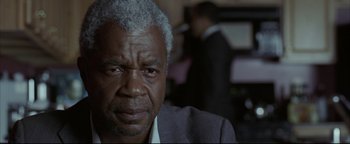 Movie still from “Syriana” (2005), directed by Stephen Gaghan – An older man in a gray suit looking at the camera; Close Up shot, Over the shoulder angle