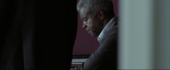 Movie still from “Syriana” (2005), directed by Stephen Gaghan – An older man in a gray suit is playing a keyboard; Close Up shot, Low angle
