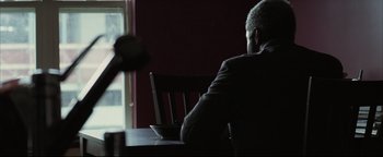 Movie still from “Syriana” (2005), directed by Stephen Gaghan – A man sitting at a table in front of a bowl of food; Medium shot, Over the shoulder angle