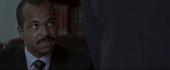 Movie still from “Syriana” (2005), directed by Stephen Gaghan – A person wearing a suit and glasses; Close Up shot, Over the shoulder angle