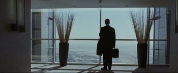 Movie still from “Syriana” (2005), directed by Stephen Gaghan – A man standing in front of a window with a briefcase; Wide shot, Low angle
