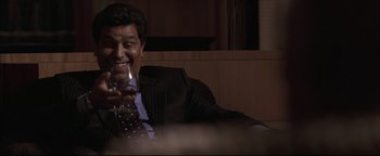 Movie still from “Syriana” (2005), directed by Stephen Gaghan – A man sitting in a chair holding a glass of wine; Medium shot, Low angle