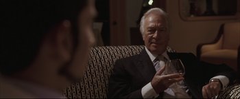 Movie still from “Syriana” (2005), directed by Stephen Gaghan – An older man wearing a suit and tie talking to a woman; Close Up shot, Over the shoulder angle