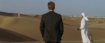 Movie still from “Syriana” (2005), directed by Stephen Gaghan – A man in a suit standing in the middle of the desert; Wide shot, High angle