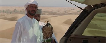 Movie still from “Syriana” (2005), directed by Stephen Gaghan – A man holding a hawk in his hand while standing next to another man; Medium shot, Over the shoulder angle