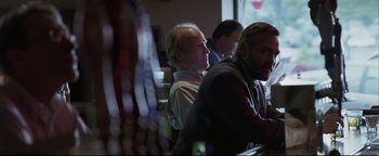 Movie still from “Syriana” (2005), directed by Stephen Gaghan – A man sitting at a table in front of a window; Medium shot, Over the shoulder angle