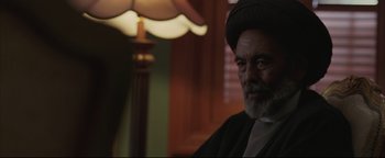 Movie still from “Syriana” (2005), directed by Stephen Gaghan – An older man sitting in front of a table lamp; Close Up shot, Over the shoulder angle