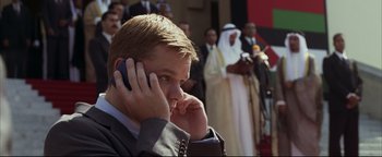 Movie still from “Syriana” (2005), directed by Stephen Gaghan – A man in a suit talking on a cell phone; Medium shot, Over the shoulder angle