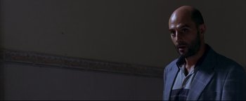 Movie still from “Syriana” (2005), directed by Stephen Gaghan – A man in a suit and tie standing next to a wall; Close Up shot, Low angle