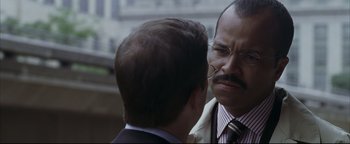 Movie still from “Syriana” (2005), directed by Stephen Gaghan – A man in a suit and tie talking to another man in a suit and tie; Close Up shot, Over the shoulder angle