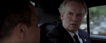 Movie still from “Syriana” (2005), directed by Stephen Gaghan – A person wearing a suit in a car; Close Up shot, Over the shoulder angle