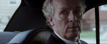 Movie still from “Syriana” (2005), directed by Stephen Gaghan – An older man in a black suit and white shirt; Close Up shot, Low angle