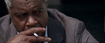 Movie still from “Syriana” (2005), directed by Stephen Gaghan – A person wearing a suit smoking a cigarette; Close Up shot, Low angle