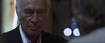 Movie still from “Syriana” (2005), directed by Stephen Gaghan – An older man in a black suit is looking at the camera; Close Up shot, Over the shoulder angle