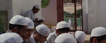 Movie still from “Syriana” (2005), directed by Stephen Gaghan – A group of men sitting in front of a building; Wide shot, Over the shoulder angle