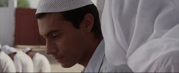 Movie still from “Syriana” (2005), directed by Stephen Gaghan – A young man wearing a white hat and a white shirt; Close Up shot, Over the shoulder angle