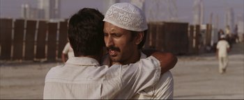 Movie still from “Syriana” (2005), directed by Stephen Gaghan – Two men are hugging each other while wearing a white hat; Close Up shot, Low angle