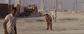 Movie still from “Syriana” (2005), directed by Stephen Gaghan – A group of men standing on top of a sandy beach; Wide shot, High angle