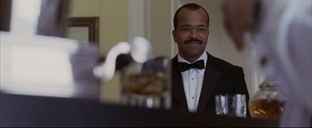 Movie still from “Syriana” (2005), directed by Stephen Gaghan – A man in a suit and bow - tie looking into a mirror; Close Up shot, Low angle