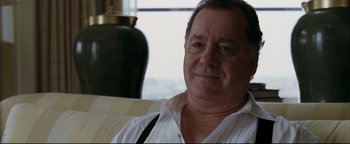 Movie still from “Syriana” (2005), directed by Stephen Gaghan – An older man wearing a white shirt sitting on a couch; Close Up shot, Over the shoulder angle