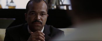 Movie still from “Syriana” (2005), directed by Stephen Gaghan – A person wearing a suit and glasses; Close Up shot, Over the shoulder angle