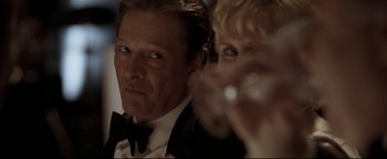 Movie still from “Syriana” (2005), directed by Stephen Gaghan – A man and a woman in formal wear looking at the camera; Close Up shot, Low angle