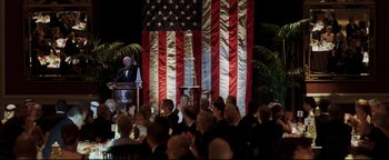 Movie still from “Syriana” (2005), directed by Stephen Gaghan – A crowd of people sitting in front of an american flag; Extreme Wide shot, High angle