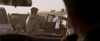 Movie still from “Syriana” (2005), directed by Stephen Gaghan – A man in a military uniform is holding a white towel; Medium shot, Over the shoulder angle