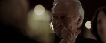 Movie still from “Syriana” (2005), directed by Stephen Gaghan – An older man is looking at the camera with his hand on his chin; Close Up shot, Low angle