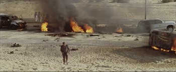 Movie still from “Syriana” (2005), directed by Stephen Gaghan – A man standing on a beach with a surfboard in his hand; Extreme Wide shot, High angle