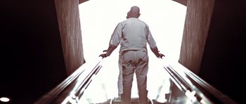 Movie still from “THX 1138” (1971), directed by George Lucas – A man standing on an escalator with his arms outstretched; Medium shot, Low angle