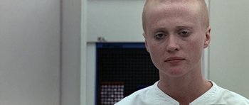 Movie still from “THX 1138” (1971), directed by George Lucas – A woman with a shaved head is looking at the camera; Close Up shot, Low angle