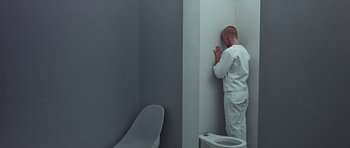 Movie still from “THX 1138” (1971), directed by George Lucas – A man in a white suit leaning against a wall in a bathroom; Wide shot, High angle