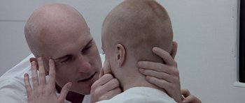 Movie still from “THX 1138” (1971), directed by George Lucas – A bald man is touching the ear of another bald man; Close Up shot, Over the shoulder angle
