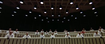 Movie still from “THX 1138” (1971), directed by George Lucas – A group of people sitting in a row in front of a stage; Extreme Wide shot, High angle