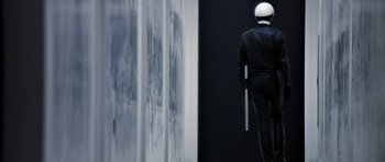 Movie still from “THX 1138” (1971), directed by George Lucas – A man in a white helmet is standing in front of a wall; Medium shot, Over the shoulder angle