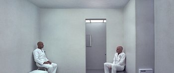 Movie still from “THX 1138” (1971), directed by George Lucas – Two men sitting in front of each other in front of a door; Wide shot, High angle