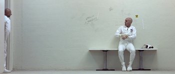 Movie still from “THX 1138” (1971), directed by George Lucas – A person sitting on a bench in a room; Wide shot, High angle
