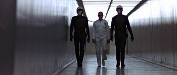 Movie still from “THX 1138” (1971), directed by George Lucas – A group of people in black and white suits walking down a hallway; Wide shot, Low angle
