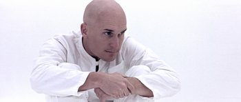 Movie still from “THX 1138” (1971), directed by George Lucas – A bald headed man in a white shirt is looking at the camera; Close Up shot, Low angle