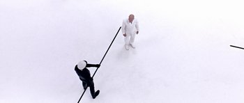 Movie still from “THX 1138” (1971), directed by George Lucas – Two men in suits and hats are standing in the middle of the snow; Wide shot, Overhead angle