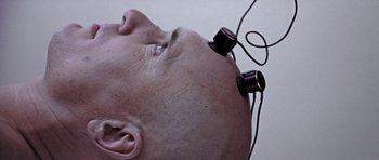 Movie still from “THX 1138” (1971), directed by George Lucas – A bald man with a pair of headphones attached to his head; Extreme Close Up shot, Overhead angle
