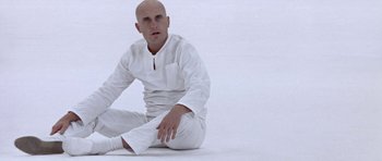 Movie still from “THX 1138” (1971), directed by George Lucas – A bald man sitting on the ground wearing all white clothes; Medium shot, High angle