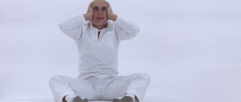 Movie still from “THX 1138” (1971), directed by George Lucas – A man sitting on the ground with his hands on his head; Medium shot, High angle