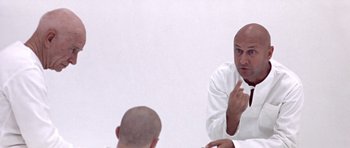 Movie still from “THX 1138” (1971), directed by George Lucas – A bald man in a white shirt is talking to another bald man; Close Up shot, Over the shoulder angle