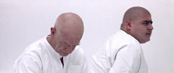 Movie still from “THX 1138” (1971), directed by George Lucas – A man in a white lab coat and a man in a white lab coat; Close Up shot, Low angle